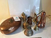 Overall view of assorted copper and brass items including bells, a pitcher, and a container.