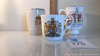 Three royal commemorative mugs placed side by side with measuring ruler behind for scale