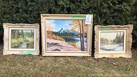 Group shot of three framed landscape paintings against hedge backdrop