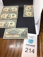 Five banknotes laid flat on black mat and wooden surface showing obverse sides.