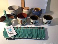 Collection of 7 ceramic pieces and a green fabric pouch holding teaspoons.
