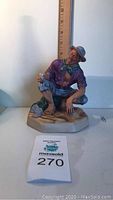 Side view of Royal Doulton 'Beachcomber C' figurine showing seated man, multi-colored ceramic.