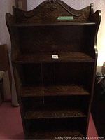 Front view of the wooden bookcase showing the ornate carved top and four shelves with vertical dividers.