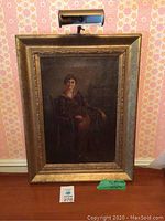 Picture of framed oil painting showing woman seated in chair, full front view with attached light.