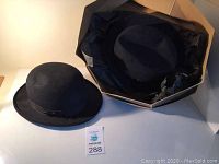 Two black vintage men's hats and the Stetson hat box on a white surface.