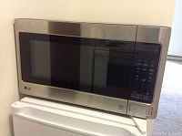 Front view of LG stainless steel microwave oven on a surface showing closed door and control panel.