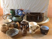 14 pieces of art pottery in grouped arrangement showing different shapes, colors, and styles on beige background
