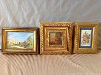 Three small framed paintings displayed side by side with different subjects and gold frames.