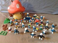 Full view of all 27 Smurf figurines arranged in front of the mushroom house along with accessory pieces