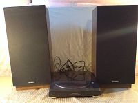 Two Fisher speakers with black grills and wooden sides, placed behind the turntable on a striped cloth surface.