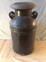 Full front view of a large antique metal milk can with two side handles and a lid.