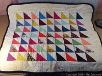 Front side of vintage crib quilt showing multicolor triangular patchwork design on cream background.
