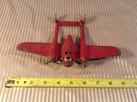 Front view of red metal airplane toy, showing twin propellers, cockpit area, and wing span measurement about 8 inches.