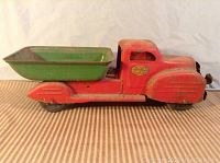 Side view of antique Lincoln Toys metal dump truck showing red cab and green dump bed with surface rust and paint loss.