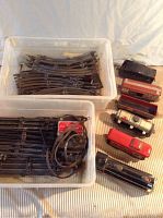 Train cars and disassembled curved and straight track pieces in plastic bins on a beige surface