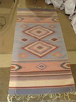 Photo of the full Mexican wool throw blanket or rug laid out flat showing geometric patterns and fringed edges.