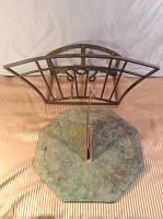 Brass hose hanger and garden sundial displayed together on fabric background.