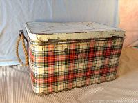 Closed plaid metal picnic box with rope handles on sides, showing exterior condition.