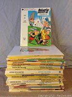 Stack of 29 Asterix comic books, spine titles visible showing various story names and authors Goscinny and Uderzo.
