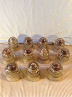 Eleven glass insulators arranged in rows on a flat surface with a white cloth background.