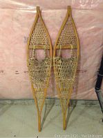 Full view of both wooden framed trapper snowshoes with traditional rawhide lacing, laid side-by-side.