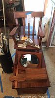 Wooden child's rocker chair placed on top of cedar chest, also wooden painted stool and oval mirror visible stacked on chest.