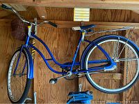 Full side view of vintage blue Roadmaster women's bicycle showing step-through frame, front wicker basket, and rear wire rack.