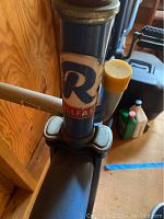 Close-up of Schwinn Rollfast badge on blue bicycle frame showing wear and rust on bolts.