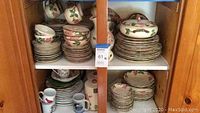 Two-shelf wooden cabinet displaying stacks of floral Desert Rose plates, bowls, cups and mugs