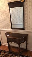 Overall view of wooden console table with single drawer and carved front, and wooden framed mirror with carved decorative detail above.