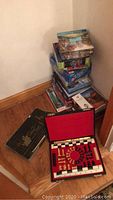 Vertical stack of assorted puzzle and game boxes, some opened and some unopened, with a chess/checkers set open in front.