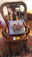 View of full rocking chair with needlepoint pillow placed on the seat showing floral stenciling on backrest and arms.