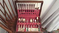 Full view of the silver plate cutlery inside an open wooden box showing knives, forks, spoons, and specialty utensils organized on red felt lining.