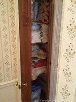 View of hallway linen closet with door partially open showing shelves filled with folded white linens and bedding items.