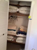 Linen closet with assorted pillows stacked on upper shelves and blankets and quilts folded on lower shelves.