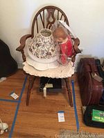 Wooden fiddleback armchair with crochet cushions, ventriloquist doll, and lampshades displayed on and around chair