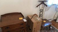 Top and partial side view of nightstand and cane resting on cardboard box, along with chair to side, showing overall lot arrangement.
