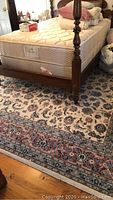 Area rug under a wooden bed frame, showing floral and medallion patterns in blue, pink, and cream colors.