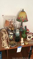 Overview of assorted decor items on wooden table including lamp, pitchers, figurines, macrame, trinket boxes, and ships.