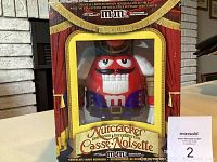 Front view of the official limited edition M&M nutcracker dispenser in original box, showing the red M&M character dressed as a nutcracker in detailed attire behind the display window.