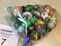 Plastic bag containing assorted glass marbles including large, small, and multicolored swirled patterns.