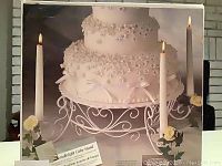 Photo of the cake stand on its original box showing the product with a decorated multi-tiered cake and lit taper candles with floral accents.