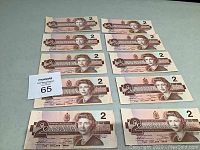 Front side of ten Canadian two dollar bills arranged in rows showing Queen Elizabeth II portrait and denomination
