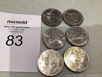 Six Canadian silver dollar coins displayed with front and back views, showing Queen Elizabeth II's profile and varying reverse designs including the Voyageur canoe and commemorative maple leaf.