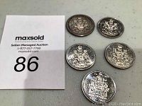 Five Canadian 50 cent coins arranged with an auction lot number card in view.