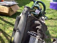 Green Yardworks electric leaf blower and vacuum unit with black collection bag sitting outdoors.