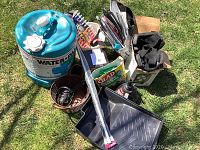 Overview of assortment including 20L Reliance Water-Pak jug, various tools, painting supplies, gloves, baskets, Christmas light clips, and household items.