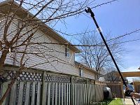 Fiskars long limb trimmer extended about 90 inches cutting tree branches high above a fence.