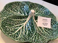 Top and side views of a large green ceramic bowl shaped into four leaf sections with a central handle, showing texture and glaze condition.