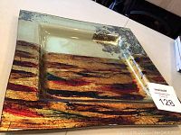 Close-up angled view of square glazed glass decorative plate with abstract multi-color design and some silver-gray accents.